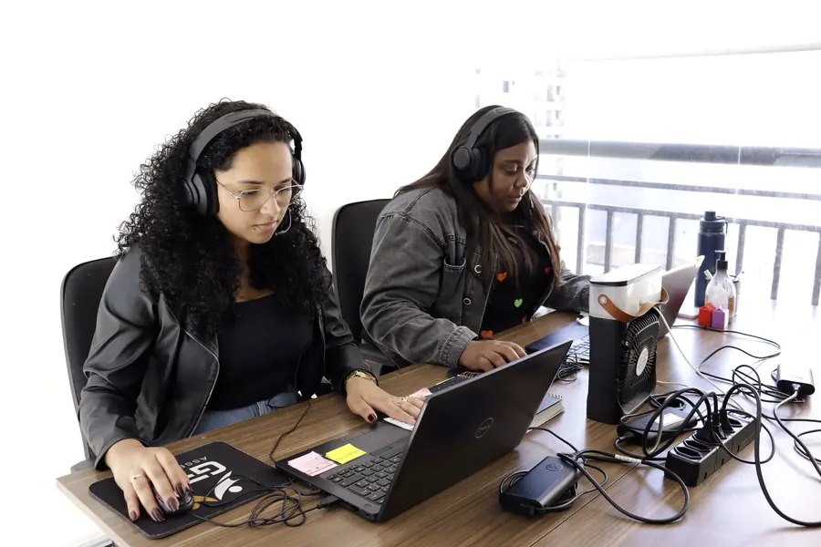 Duas atendentes da GPM de headset, trabalhando no notebook