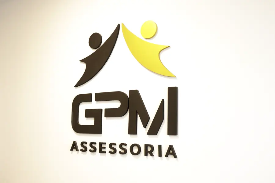 Logo da GPM Assessoria, com o símbolo das duas figuras, na parede branca do escritório